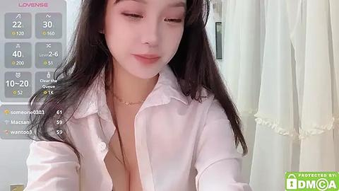 Media: Video of a young Asian woman with long black hair, wearing a white blouse unbuttoned to reveal cleavage, in a room with a calendar and curtains.