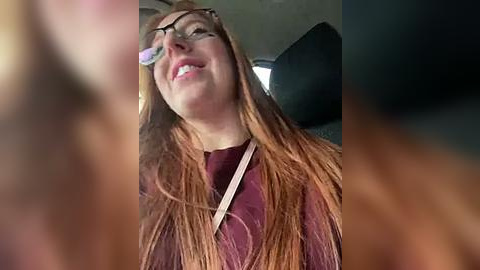 Media: A video of a smiling woman with long red hair and glasses, wearing a maroon sweater, seen from the driver's perspective.