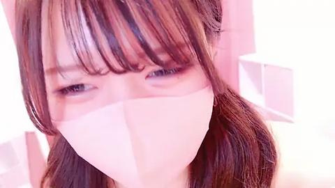 Media: Video of an Asian woman with long, straight brown hair, wearing a surgical mask, taken indoors with soft, pastel lighting.