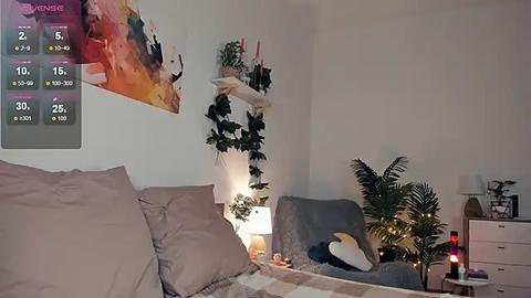 Media: Video of a cozy, modern bedroom with a gray bed, hanging plants, a potted palm, a blue armchair, and a colorful abstract painting on the wall.