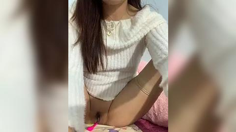 Media: Video of a young Asian woman with long brown hair, wearing a white knit sweater and beige thigh-high stockings, sitting on a pink bed.