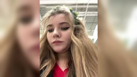 Media: Video of a young woman with long, blonde hair in a messy, tousled style, wearing a red shirt, captured from a slightly blurred, close-up angle.