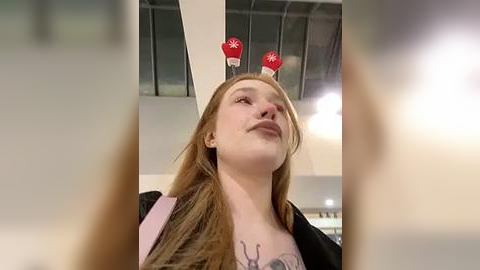 Media: A video of a fair-skinned, red-haired woman wearing red antlers and a pink jacket, standing in a modern indoor space with glass ceilings.