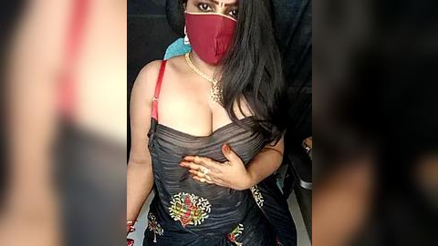 Media: Video of a curvy woman with long black hair, fair skin, and large breasts, wearing a red face mask, dark denim overalls, and gold jewelry.