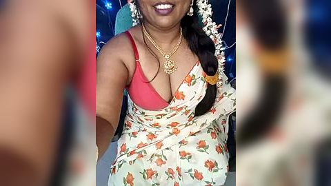 Media: A video of a smiling South Asian woman with medium-dark skin, wearing a red bra under a floral sari, adorned with gold jewelry and a garland of white flowers.