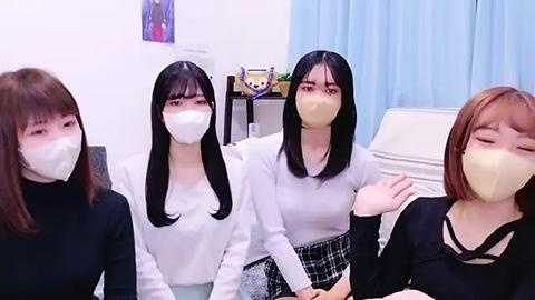 Media: Video of four Asian women wearing surgical masks, seated in a hospital room with light blue curtains and a white chair, with a potted plant and a toy bear on a shelf in the background.