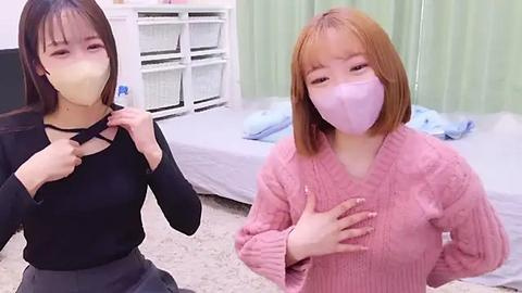 Media: Video of two young Asian women wearing face masks, one adjusting a black choker, the other in a pink sweater, standing in a simple bedroom with white shelves and a bed.