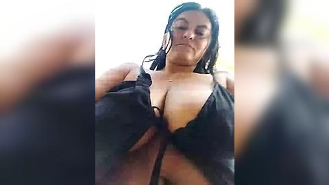 Media: Video of a woman with wet, dark hair, wearing a black bra, looking downward. The background is blurred.