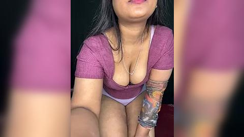 Media: Video of a young woman with medium skin tone, long black hair, and a tattooed arm, wearing a tight, low-cut maroon top revealing cleavage, and light purple panties.