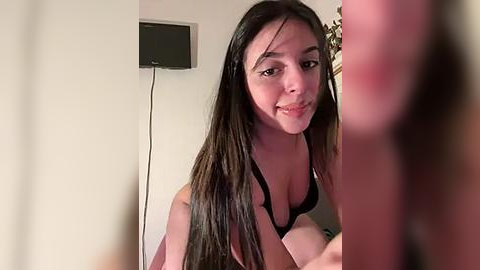 Media: Video of a young woman with long dark hair, fair skin, and a slender build, wearing a black bra, smiling in a dimly lit bedroom.