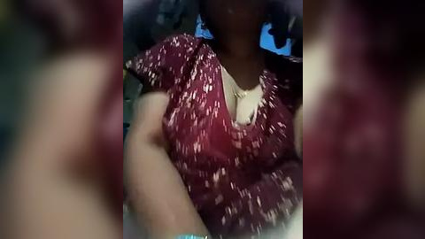 Media: Video of a person with medium-dark skin tone wearing a maroon blouse with white polka dots, seated in a car with blurred background.