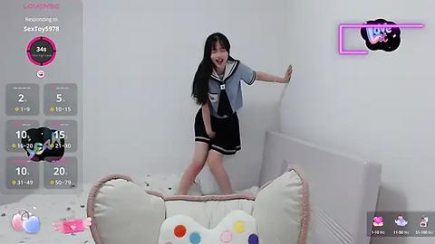 Media: A video of a young Asian woman in a light blue shirt and black skirt, joyfully jumping in a pink, plush cat bed in a minimalist white room with a neon \"KU\" sign.