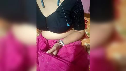 Media: Video of a woman wearing a black top and bright pink sari, seated on a pink bed with a blue stethoscope around her neck.