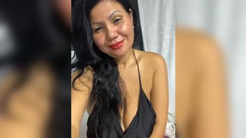 Media: Video of an Asian woman with long black hair, smiling, wearing a black halter top, against a blurred background.