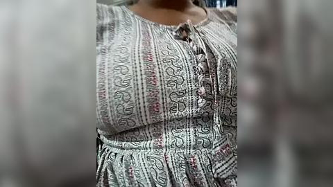 Media: A video of a woman in a patterned, floral-print dress with a buttoned front, standing indoors. The background is blurred, focusing on the dress details.