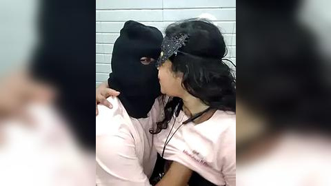 Media: Video of two women in a bathroom, one wearing a black mask, kissing passionately. The woman in the mask has a large bust and the other has long dark hair.