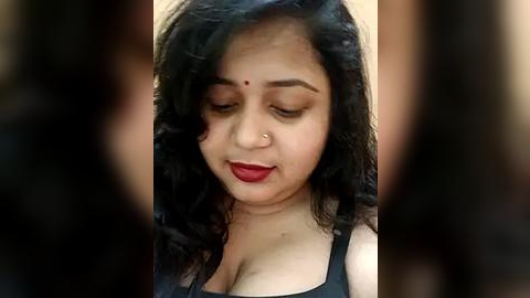 Media: Video of a South Asian woman with long black hair, fair skin, and red lipstick. She has a nose ring and is wearing a black top.