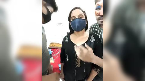 Media: Video of a woman with a blue mask, black top, and brown hair, being restrained by two men in a crowded, dimly lit room.