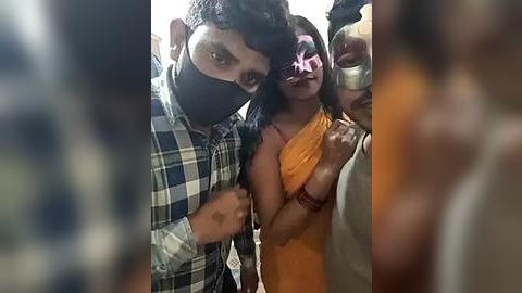 Media: Video of a young man with short dark hair in a plaid shirt, a woman with long dark hair in a colorful orange saree, and two others in a festive, possibly Holi celebration setting.