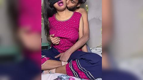 Media: Video: A woman with long black hair, wearing a red blouse, and a man with short brown hair, both in a bedroom, embracing intimately.