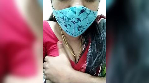 Media: Video of a woman with a blue surgical mask and a red blouse, wearing a gold necklace, being comforted by a man in a red shirt.