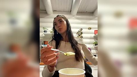 Media: A video of a woman with long dark hair in a white sweater eating ice cream in a rustic, white-paneled room with wooden beams.