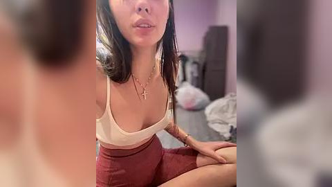 Media: A candid video of an Asian woman with medium-length dark hair, wearing a low-cut white top and high-waisted red skirt, sitting on a bed in a softly lit bedroom.