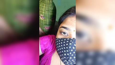 Media: Video of a woman with brown skin, wearing a green checkered mask, pink sari, and black patterned mask, with a blurred background.