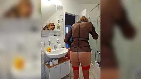 Media: Video of a woman in a bathroom, wearing a sheer black top and red lingerie, with a mirror reflecting her face, and a towel on the floor.