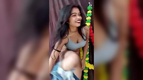 Media: Video of a joyful, dark-skinned woman with long black hair, wearing a light blue tank top and traditional necklace, dancing energetically.