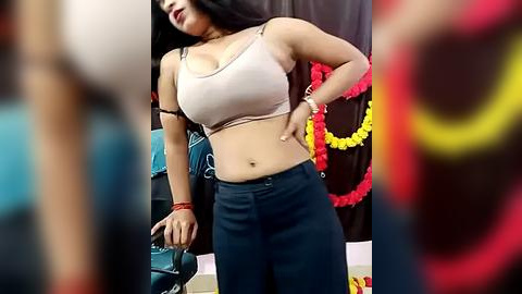 Media: Video of a curvaceous woman with long black hair, wearing a beige bra and high-waisted jeans, standing indoors with festive decorations in the background.