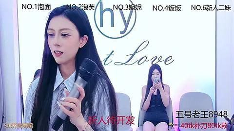 Media: Video of a slim, East Asian woman with long black hair, wearing a grey striped shirt, holding a glass. Background shows another woman seated, holding a phone. Chinese text and numbers are present.