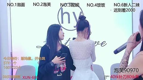 Media: Video of two East Asian women at a press conference; one in a black blazer, the other in a white lace dress, with a backdrop featuring \"hy\" logo.