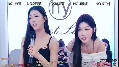 Media: Video of two young Asian women with long black hair, wearing off-shoulder white tops, speaking into microphones, with a backdrop featuring \"NYLON\" logo and blurred audience members.