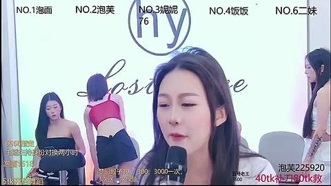 Media: Video of an Asian woman with long black hair, wearing a white top, speaking into a microphone in a studio setting. Background features models in red and black lingerie, with Chinese text and brand logos.