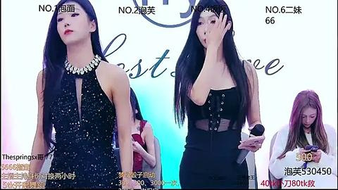 Media: Video of a slender East Asian woman in a black sequin dress and a second woman in a black lace outfit, both on a white stage with a \"Best Dressed\" backdrop.