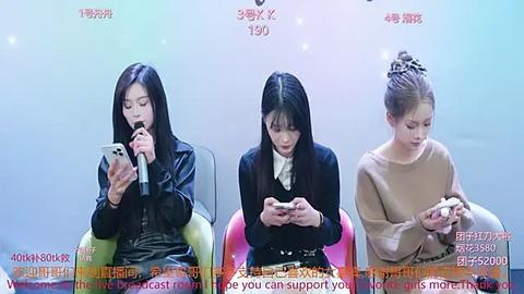 Media: Video of three young East Asian women seated, each holding a smartphone, dressed in casual attire, against a light blue background.