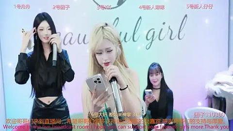 Media: Video of a live performance with three women on stage, two holding microphones, one with long blonde hair, one with black hair, and one with black hair.