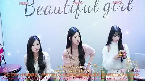 Media: Video of three young Asian women with long black hair, wearing casual outfits, seated at a table in a studio setting.