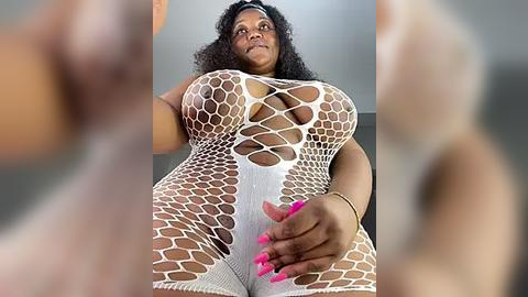 Media: Video of a curvy, Black woman with curly hair, wearing a white fishnet bodysuit that reveals her large breasts and ample hips, standing in a low-angle shot, with blurred figures in the foreground.