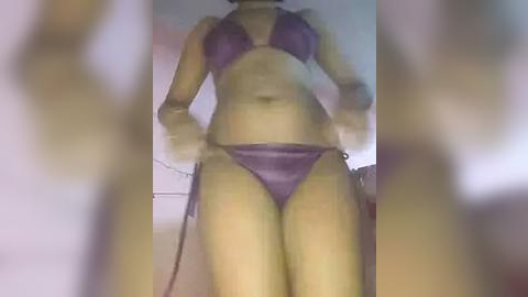 Media: A blurred video of a woman in a purple bikini, seen from a low angle. The background features a light-colored room with minimal decor.