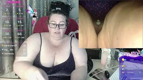 Media: Video of a plus-sized, fair-skinned woman with glasses, wearing a dark tank top, sitting in a red chair; close-up of her large breasts, and a video overlay of her webcam feed.