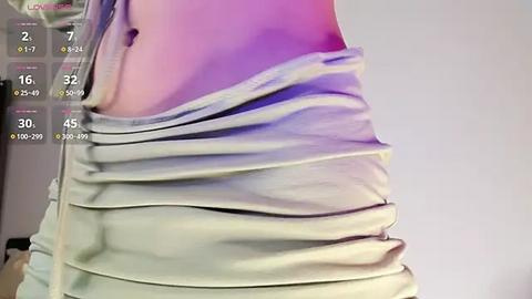 Media: A close-up video of a person's lower torso, wearing a light gray, ruffled tank top, revealing a smooth, fair-skinned stomach. The background is a plain, light-colored wall.