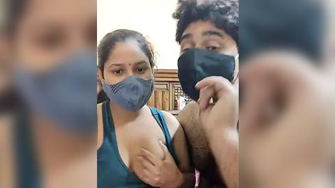 Media: A video of two people, a woman with a blue mask and blue tank top, and a man with a black mask, standing close together indoors.