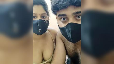 Media: Video of two South Asian women with medium skin tones, wearing black masks and light-colored tops, standing close together, with a blurred background.