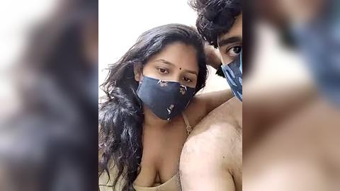 Media: Video of a South Asian woman with medium skin tone, wearing a black face mask and a beige top, captured from a close-up angle.