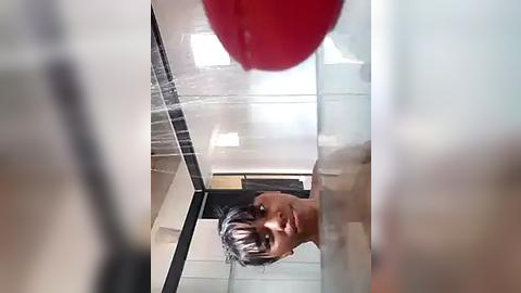 Media: A video of a young man with short black hair, shirtless, looking up while holding a red punching bag in a modern gym.