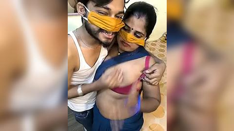 Media: Video of a smiling South Asian man in a white tank top, holding a woman in a red bra, blue shorts, and yellow mask, in a colorful room.