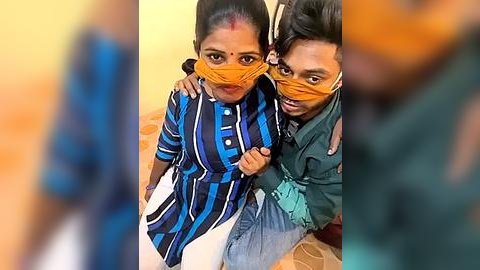 Media: Video of two young Indian girls with dark skin, wearing orange face masks, striped blue and white dresses, and seated on a tiled floor.