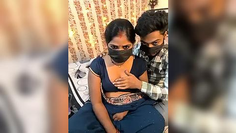 Media: Video of a young woman with dark skin and medium build, wearing a black mask, sitting on a bed with a man behind her, both wearing casual clothes.